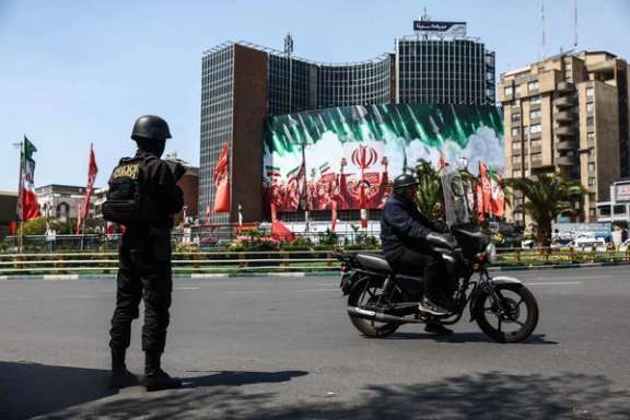 A police officer stands guard as a motorcyclist passes a large billboard depicting Iranian missiles in central Tehran, April 1, 2026