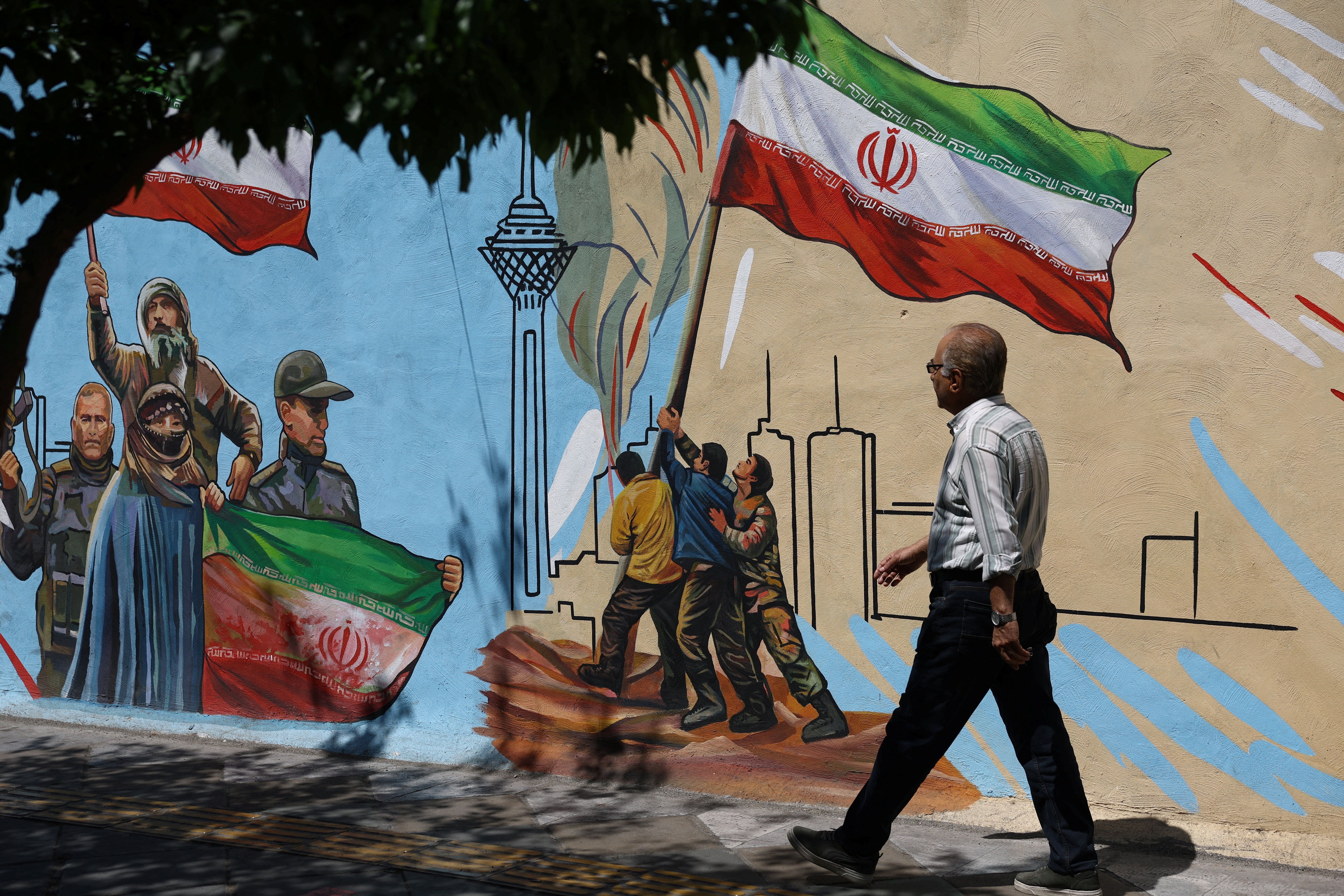 An Iranian man walks next to a mural on a street in Tehran, Iran, May 11, 2026.