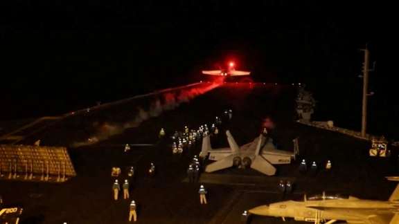 A US warplane taking off from an aircraft carrier during a nighttime operation.