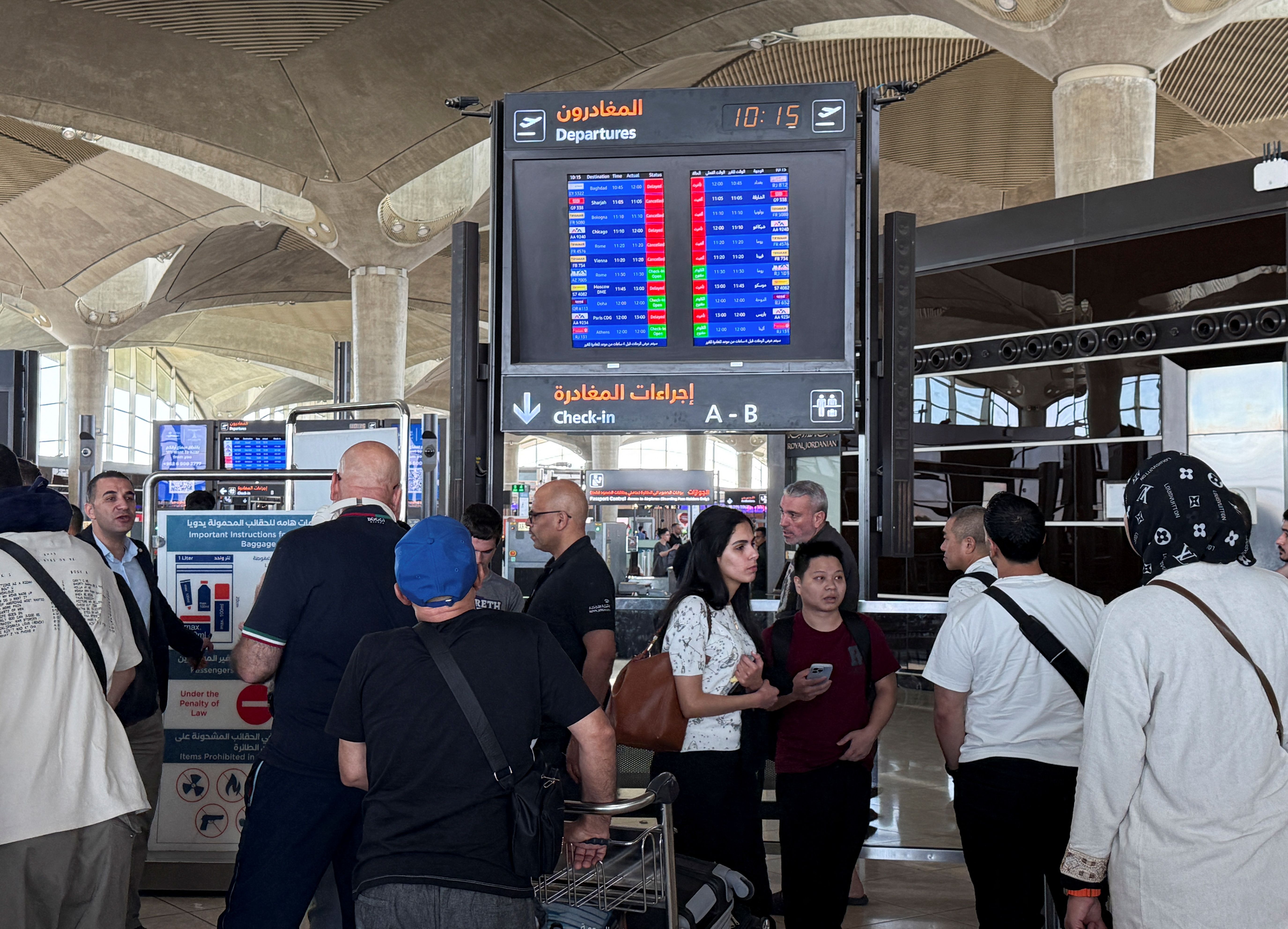 People stand in front of a flight information display screen showing information about delayed and cancelled flights, at Queen Alia International Airport in Amman, Jordan June 13, 2025. 