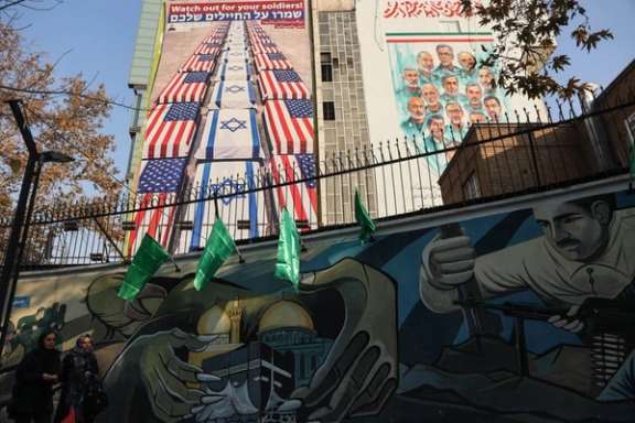People walk past murals and a banner in central Tehran showing coffins wrapped in Israeli and US flags