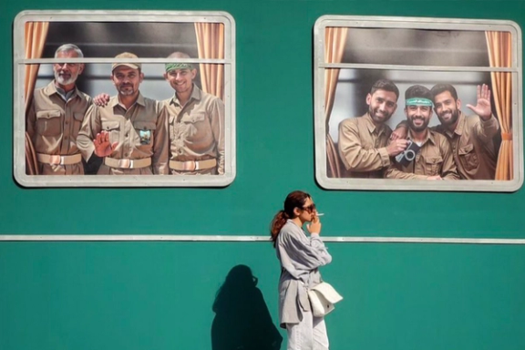 A woman walks past state-sanctioned war imagery in Tehran without the compulsory hijab