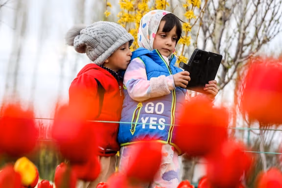 Children look at a mobile device among spring tulips in a flower garden in Tabriz, northwestern Iran, May 24, 2026