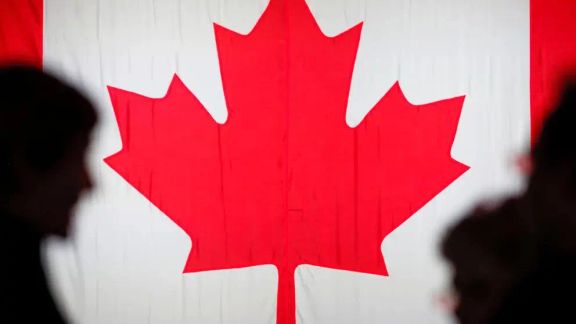 People are silhouetted in front of the Canadian national flag in Montreal, Quebec, Canada.