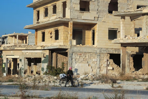 A man walks with his bike past damaged buildings in the town of Tel Rifaat, Syria December 2, 2024.