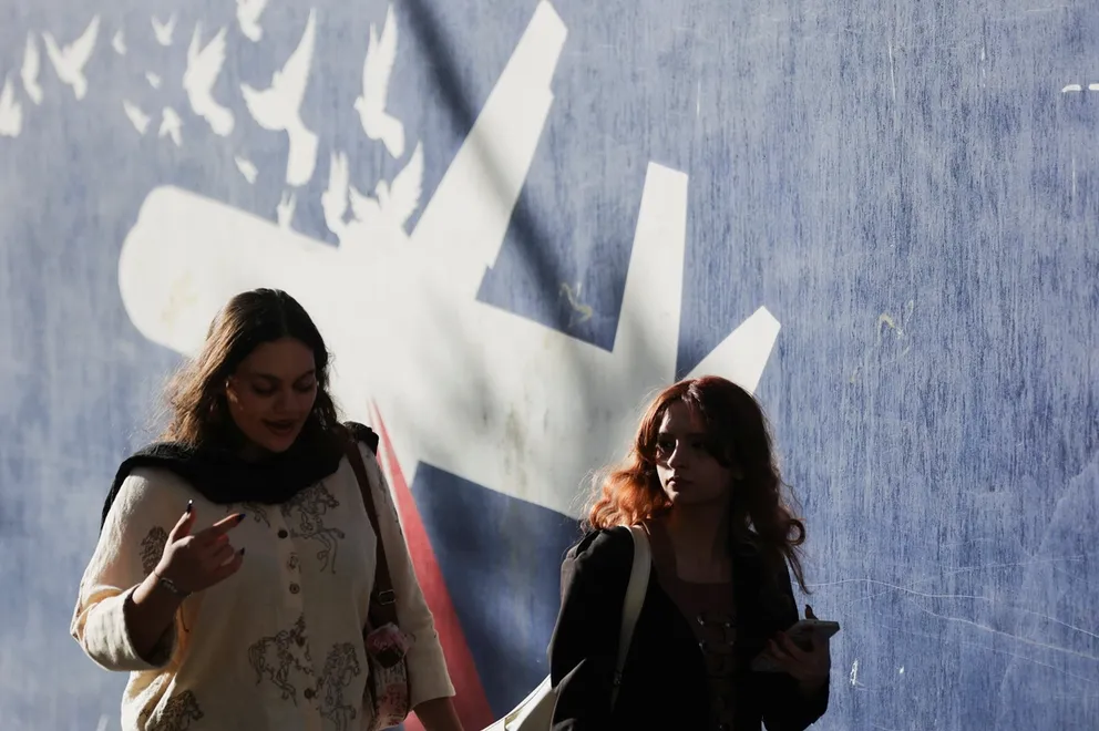 Iranian women walk past an anti-US mural on a street in Tehran, Iran, October 14, 2025.