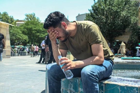 A young man cools off by a fountain during a heatwave in Iran, using bottled water to combat the temperatures