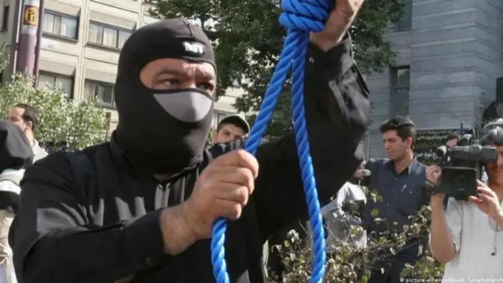 A masked executioner prepares a noose for a public hanging in Iran