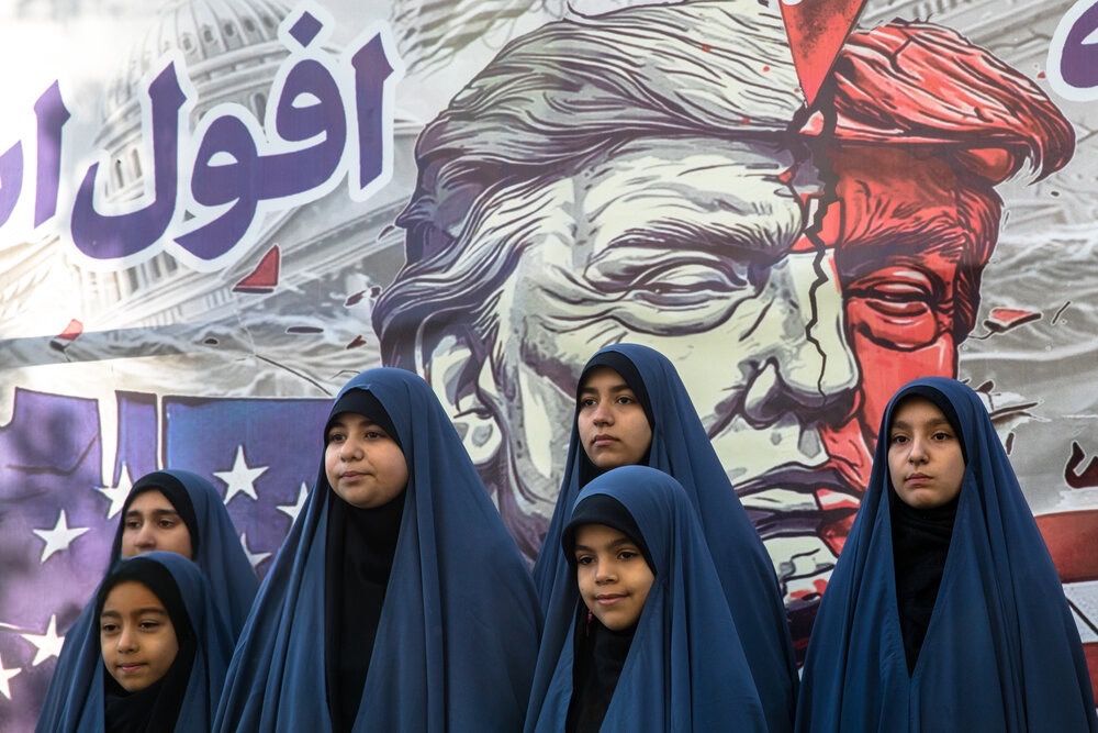 Students in black chadors pose in front of a mural of US president Donald Trump on the sidelines of a state-sponsored rally to mark the seizure of the US embassy in Tehran after the 1979 Revolution, November 5, 2025