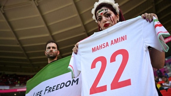 Two Iranian fans holding a jersey in memory of Mahsa Amini, whose death in custody sparked the ongoing protests, and a flag with the main motto of the protests before they were confronted by the Qatari police