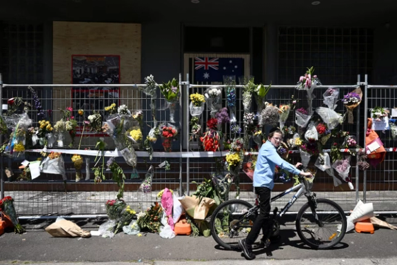 A boy on a cycle looks on next to floral tributes and an Australian flag at the Adass Israel Synagogue after an attack in Melbourne, Australia, December 10, 2024.