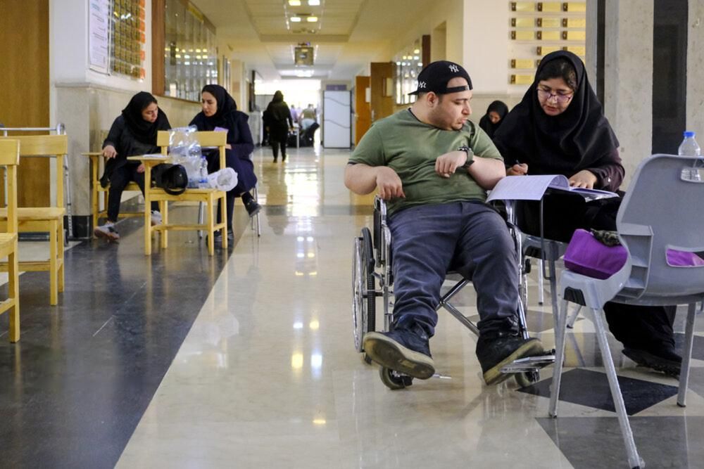 A young man in a wheelchair is assisted with paperwork in a public building in Iran.