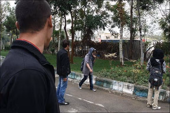 Two young women walk along a sidewalk while being closely watched and harassed by some men.