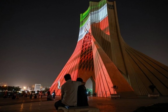 A couple sits at the foot of Tehran's iconic Azadi monument, lit by the three colours of Iran's flag, June 25, 2025