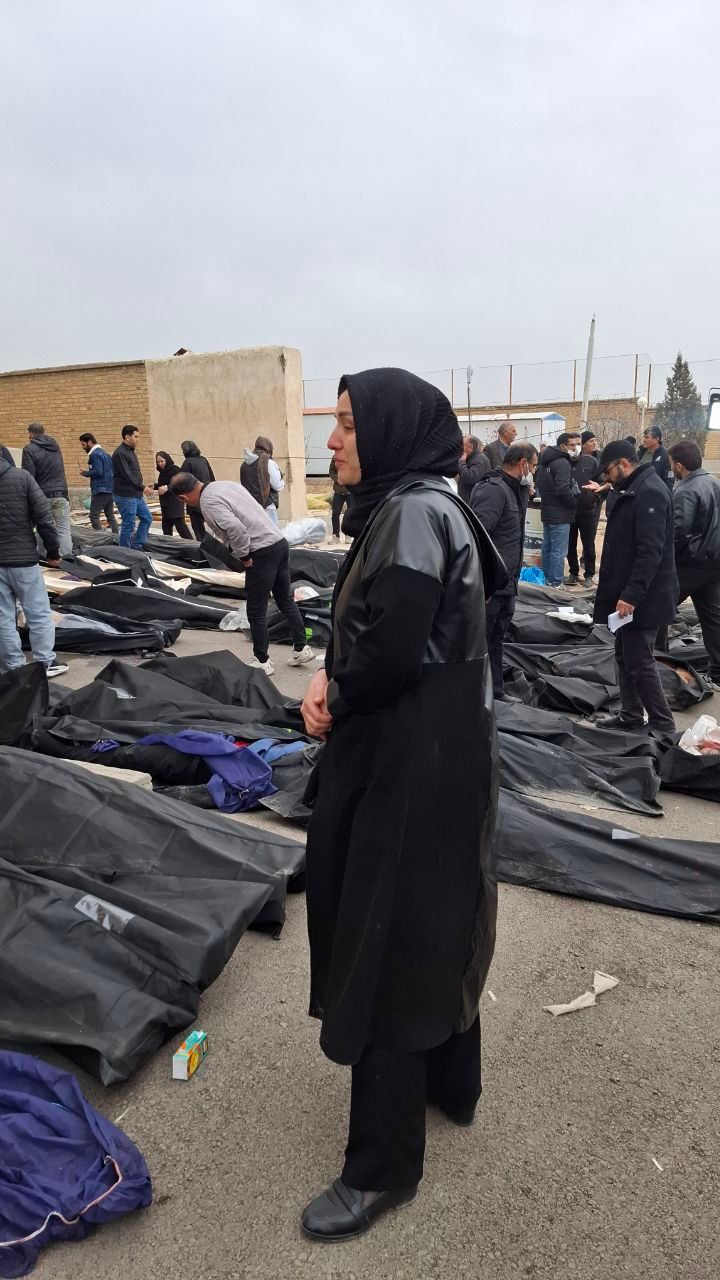 A woman stands among body bags as families gather at a facility to collect the bodies of loved ones killed during protests. (January 2026)