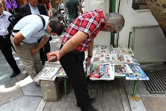 People browsing newspaper headlines at a newsstand on the streets of Tehran.