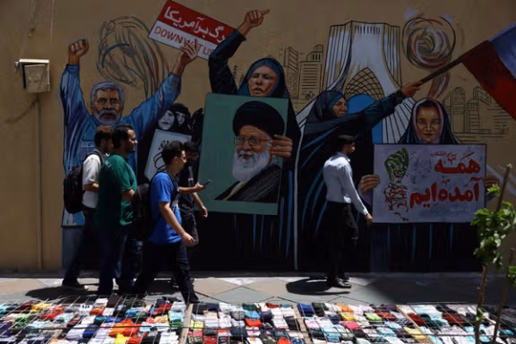 People walk on a street near a mural featuring an image of the late Supreme Leader Ali Khamenei, in Tehran, Iran, May 6, 2026.