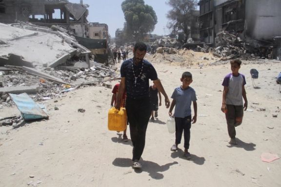 آوارگان فلسطینی در حال حمل ظروف آب در میان ویرانههای اردوگاه جبالیا، شمال نوار غزه، ۱۹ خرداد