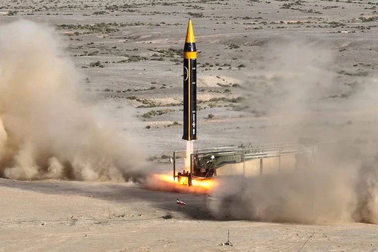 An Iranian ballistic missile launches from a desert test site, sending clouds of dust and smoke into the air.