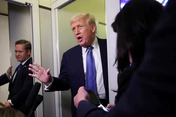 US President Donald Trump speaks to reporters, watched by National Security Advisor Mike Waltz, aboard Air Force One on his return to Washington, DC, March 16, 2025.