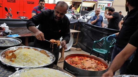 A man serves hot rice and stew to pilgrims during Arbaeen, offering free votive food.