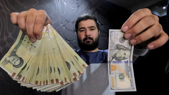 A money changer poses for the camera with a US hundred dollar bill (R) and the amount being given when converting it into Iranian rials (L), at a currency exchange shop in Tehran's business district, Iran, January 20, 2016.