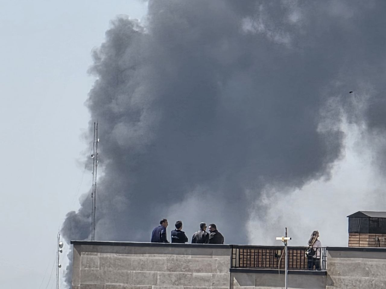 Residents watch as a large plume of smoke rises over Tehran following Israeli-US strikes (undated).
