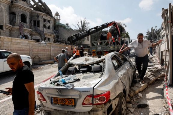 Men walk near a damaged vehicle at an impact site following missile attack from Iran, in northern Israel, in Tamra, Israel, June 15, 2025.