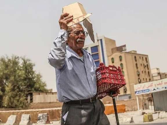 An elderly man shields himself from the scorching sun with a piece of cardboard amid a heatwave in Iran