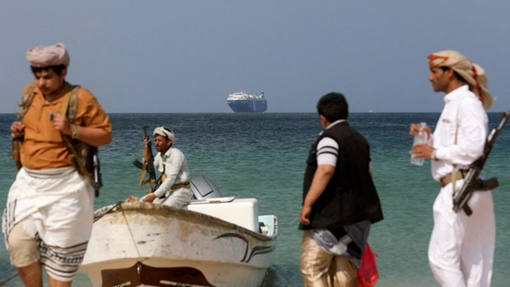 Armed men stand on the beach as the Galaxy Leader commercial ship, seized by Yemen's Houthis, is anchored off the coast of al-Salif, Yemen, December 5, 2023.