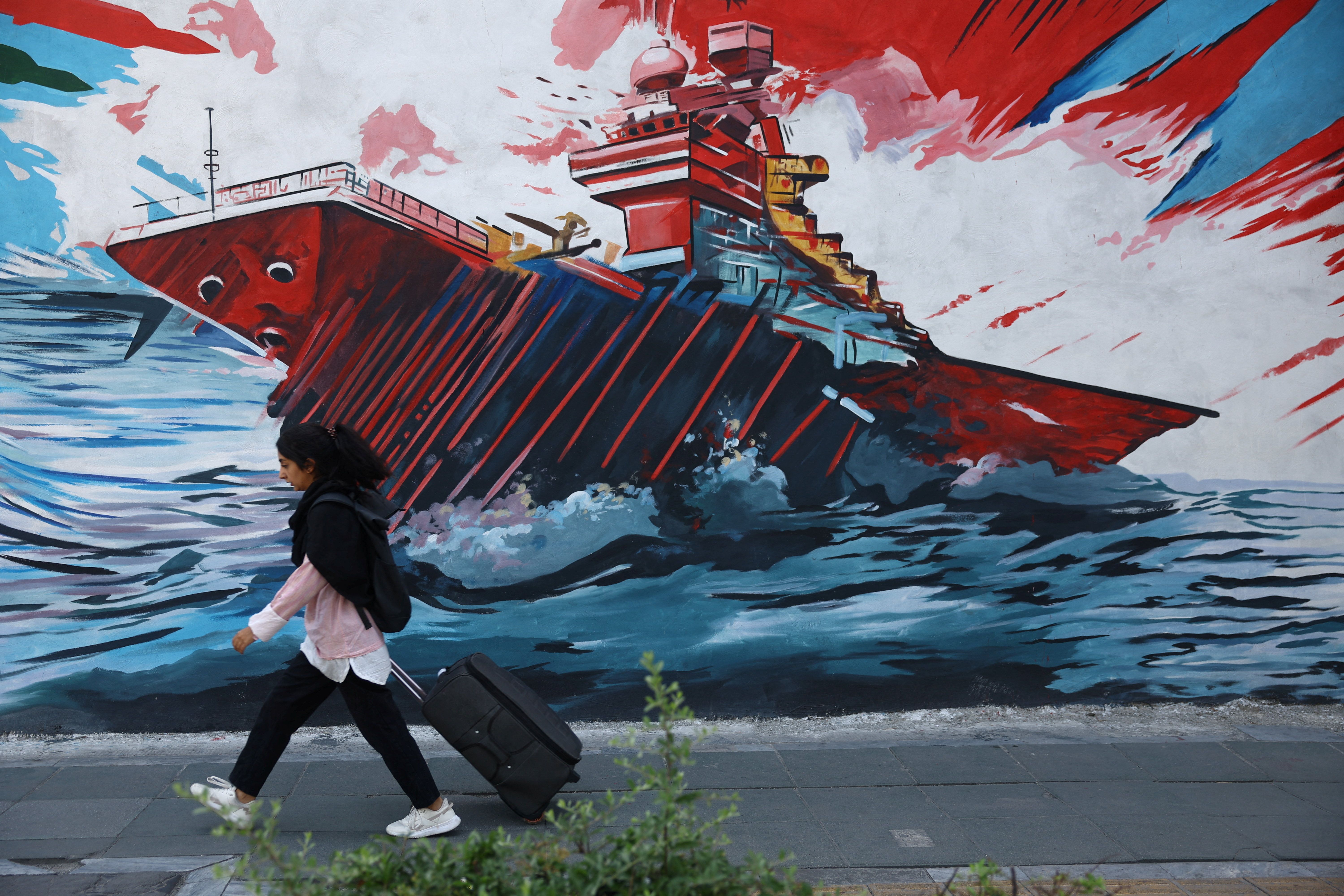 An Iranian woman walks next to a mural on a street in Tehran, Iran, May 11, 2026. 