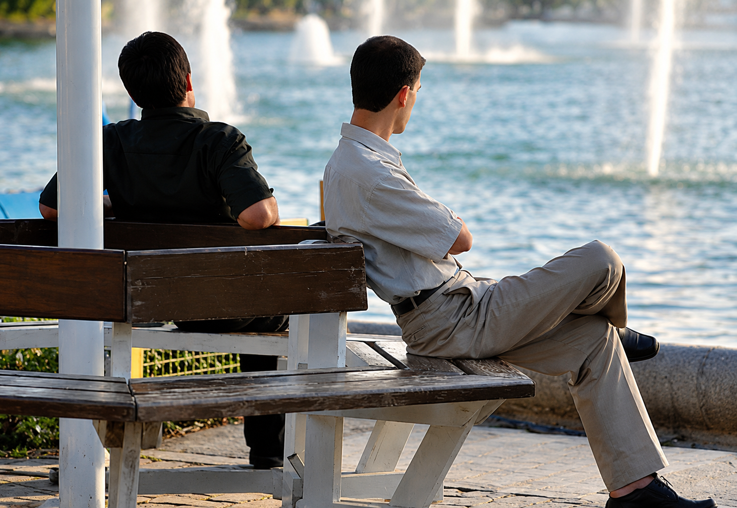 Two men sit beside a fountain in an Iranian park.