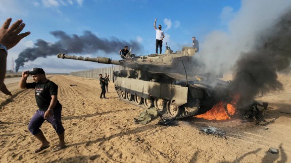Palestinians celebrate by a destroyed Israeli tank at the Gaza Strip fence east of Khan Younis, October 7, 2023.