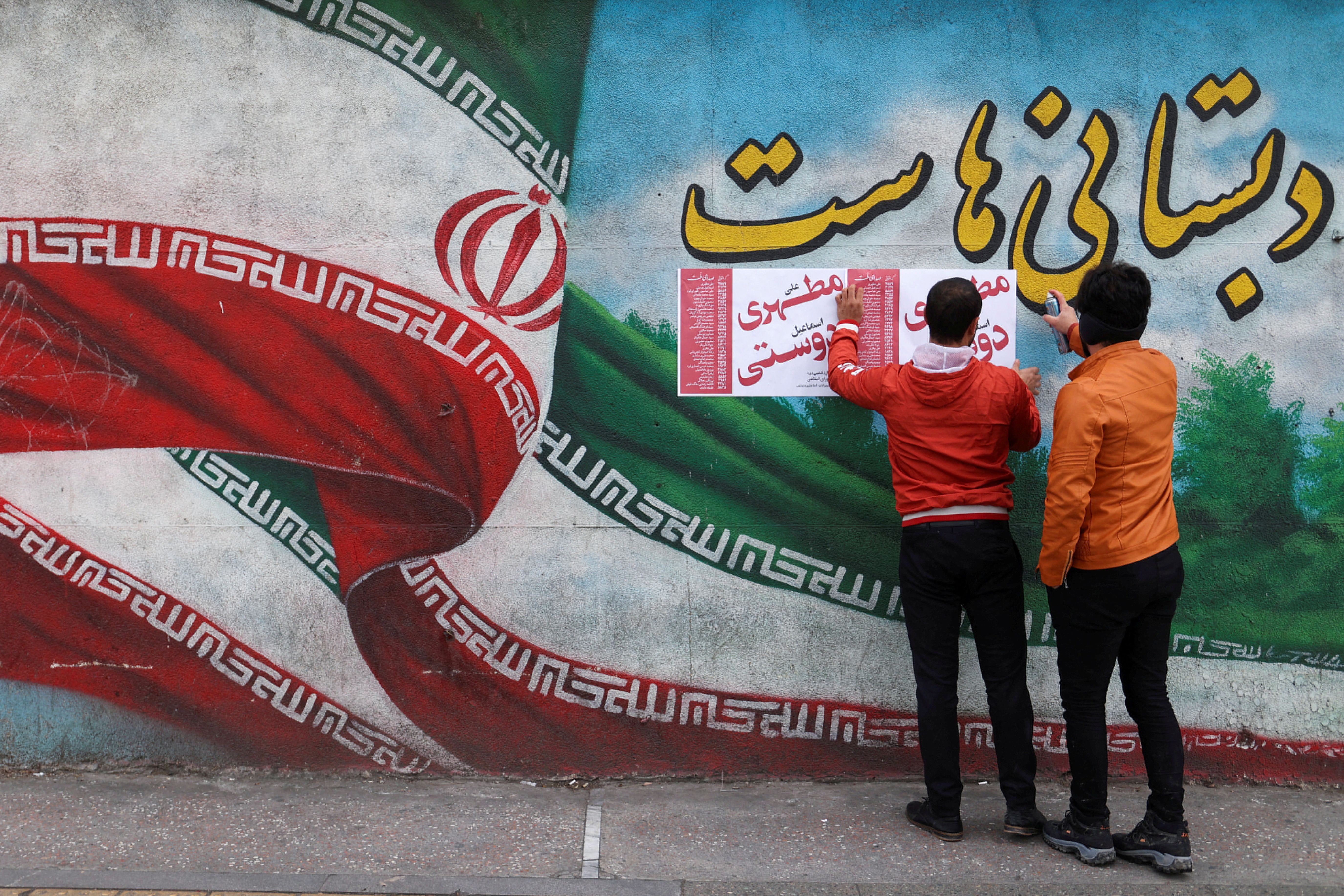 Iranian men put campaign posters on a wall during the last day of election campaigning in Tehran, Iran, February 28, 2024.