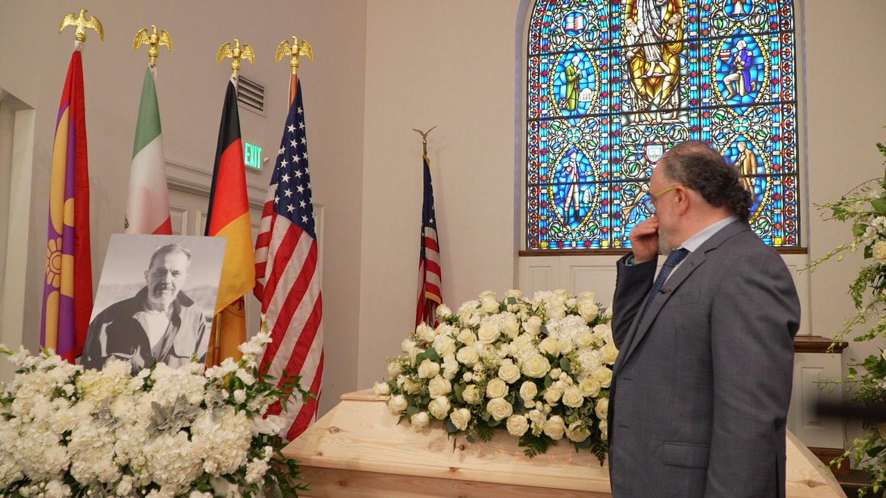 Iran International journalist Ardavan Roozbeh, director of the documentary I'm Fine, I'll Call You!, stands beside the coffin of Iranian-German dissident Jamshid Sharmahd during his funeral service.