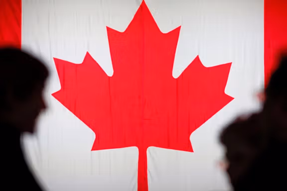 People are silhouetted in front of the Canadian national flag in Montreal, Quebec, Canada.