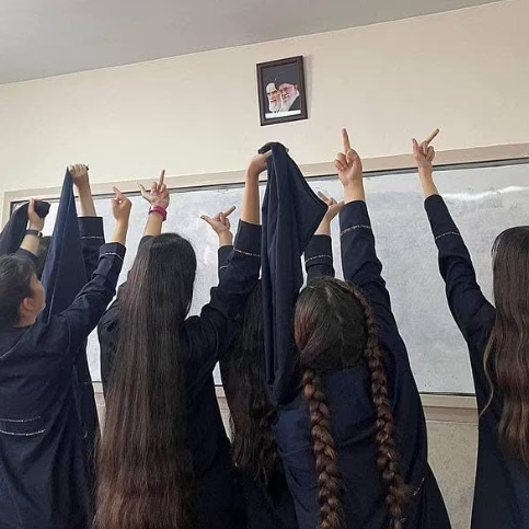 Iranian schoolgirls raising their middle fingers at a portrait of Iran's leaders in a classroom.