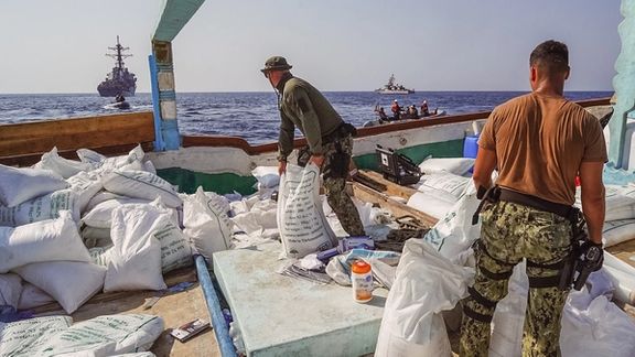 Guided-missile destroyer USS The Sullivans (DDG 68) and patrol coastal ship USS Hurricane (PC 3) sail in the background as Sailors inventory a large quantity of urea fertilizer and ammonium perchlorate discovered on board a fishing vessel intercepted by U.S. naval forces while transiting international waters in the Gulf of Oman, November 9, 2022.