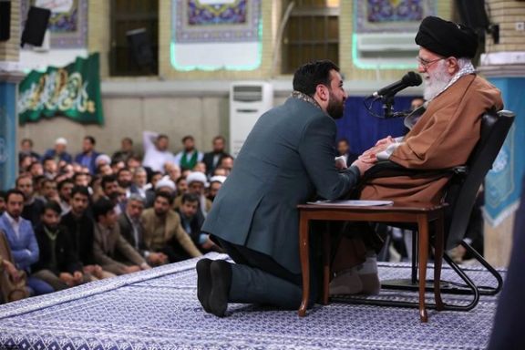 A maddah kneeling on front of Khamenei tokiss his hand