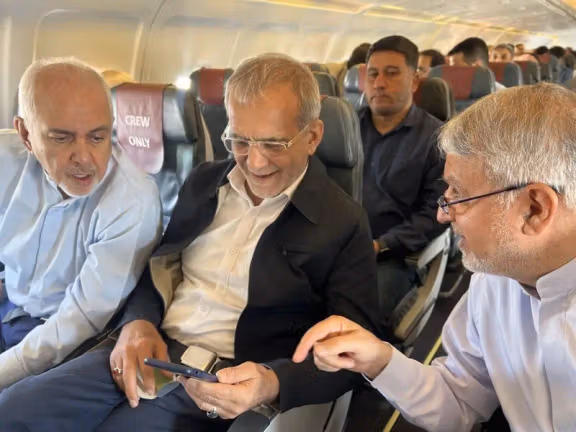 Iranian President Masoud Pezeshkian is seen seated on a plane, surrounded by other officials, including former Foreign Minister Mohammad Javad Zarif (left).