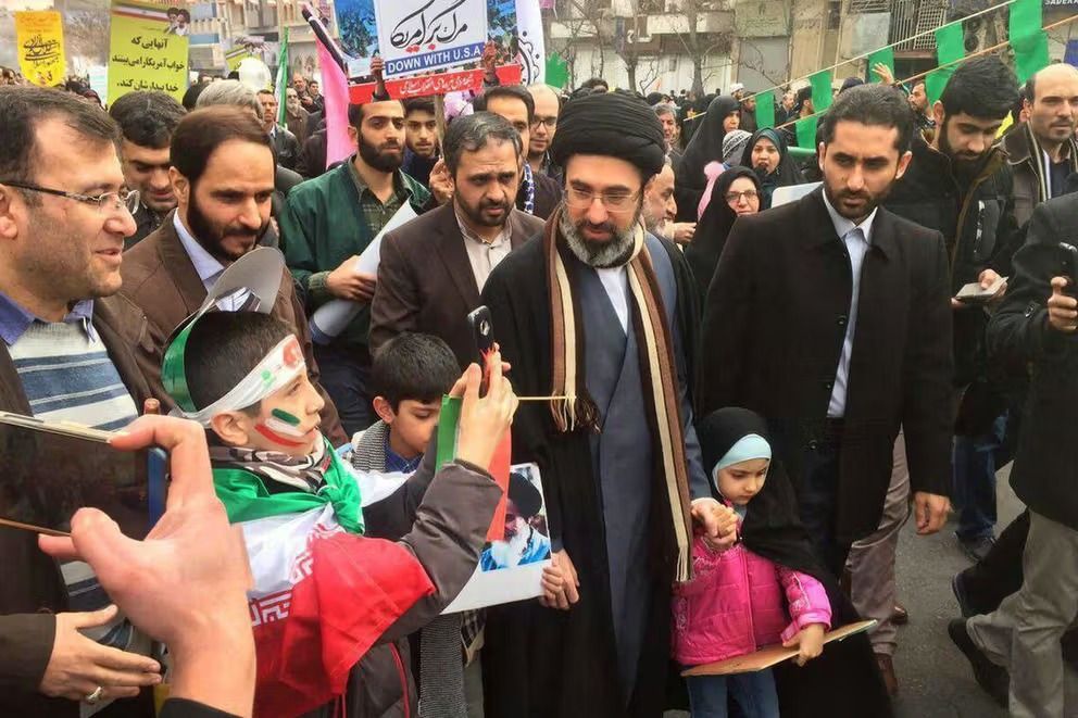 Mojtaba Khamenei attends a pro-government rally in Tehran, surrounded by supporters waving Iranian flags and anti-US banners.
