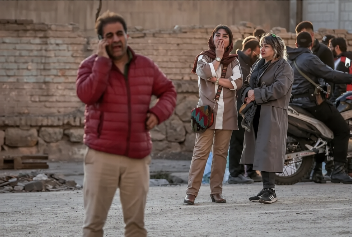 Civilians react on a street as tensions rise during the US–Israeli conflict with Iran, with one man speaking on the phone while others look on in concern.