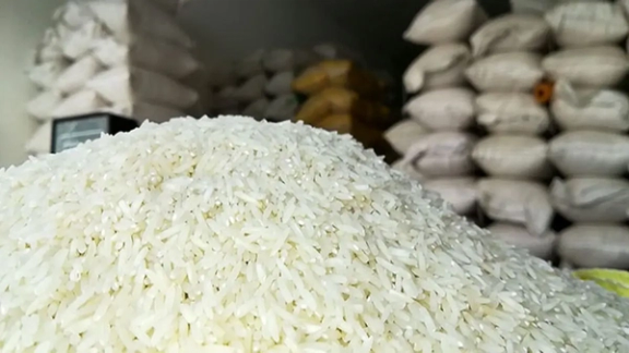 A pile of rice with stacked bags of rice in the background, in a warehouse in Iran. (Undated)