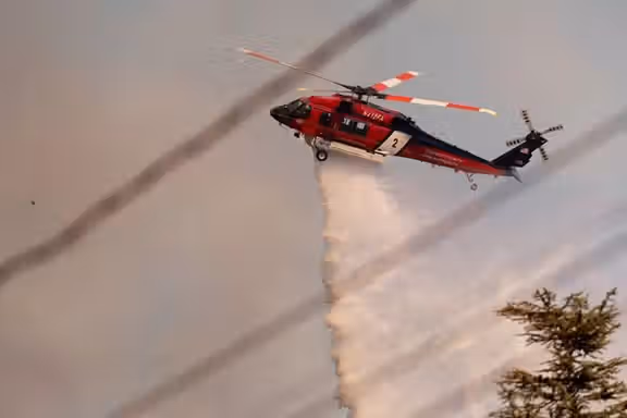 A helicopter drops water on the Palisades Fire, one of several simultaneous blazes that have ripped across Los Angeles County, along Mandeville Canyon, in the Encino neighborhood of Los Angeles, California, US, January 11, 2025.