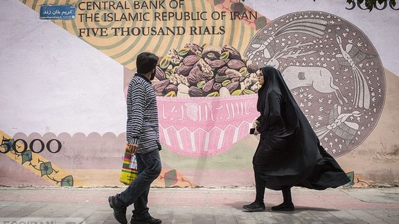 A man and a woman walking in front of a mural of a 5,000-rial banknote (now worth about one cent) in Tehran. Unlike the original design, the bowl in the mural is full of nuts whose price ranges between 5,000,000 to 100,000,000 rials (about $10 to $20) in the market.