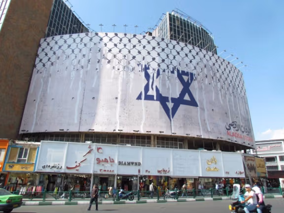 People walk past an anti-Israel billboard with the chequered Keffiyeh covering the Star of David in Tehran's central Vali-Asr square. (October 2023)