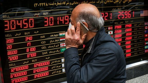 File photo of an Iranian man passing in front of a board that shows exchange rates against rial