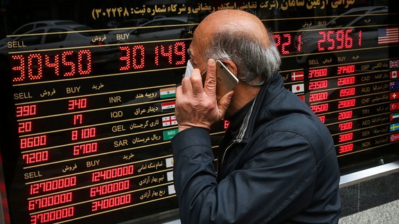 File photo of an Iranian man passing in front of a board that shows exchange rates against rial