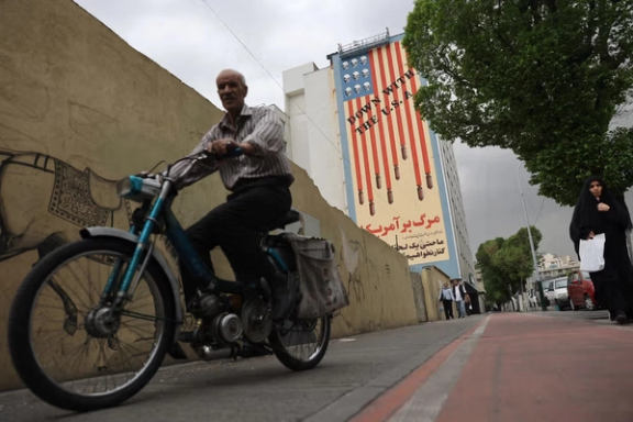 A man rides a motorbike past a mural in Tehran,depicting the US flag with skulls and bombs, alongside the anti-American slogan “Death to America.”