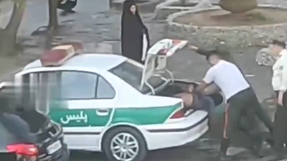 Police officers in Iran forcefully cram a person into the trunk of a police car, as captured in a video circulated on social media